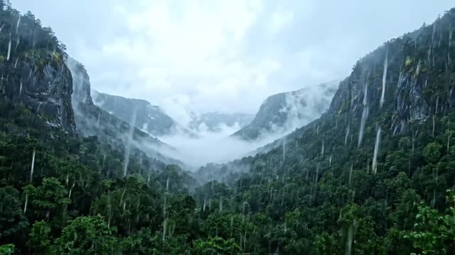 A slow rise above a misty valley as rain falls through grey cloud