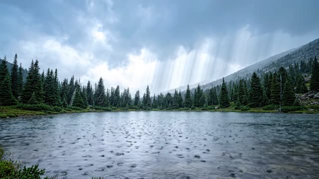 A high alpine lake ringed by dark pines under rain cloud