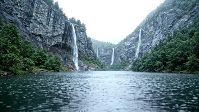 A narrow fjord with waterfalls streaming down dark cliffs in rain