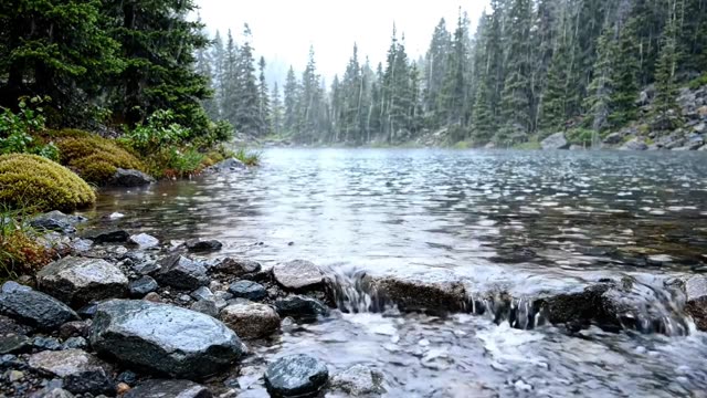A mountain lake outlet spilling over smooth rocks in rain